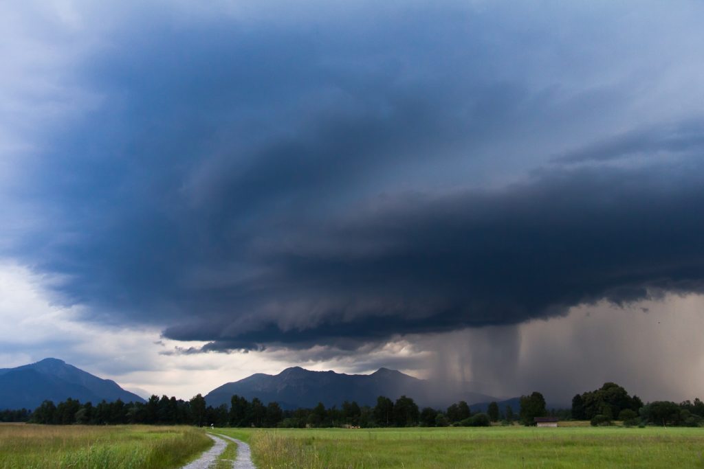 Une prairie avec d'énormes nuages noirs dans le ciel au dessus des montagnes situées en arrière plan